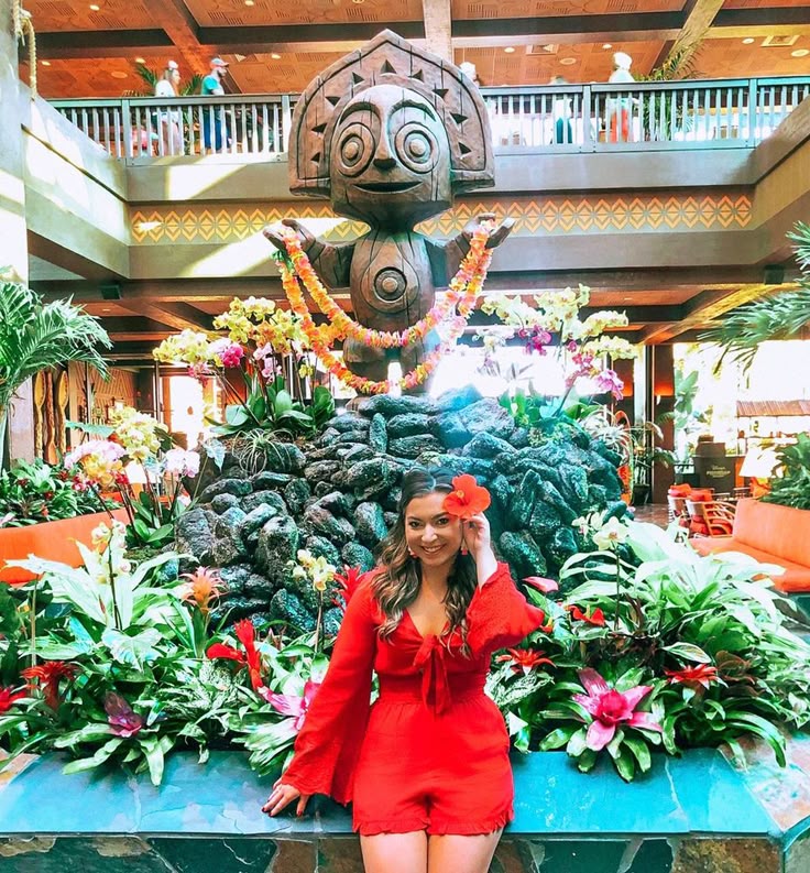 This may contain: a woman in a red dress posing for the camera with flowers and plants around her