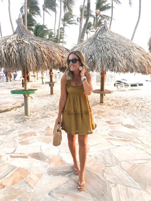 This may contain: a woman is standing on the beach talking on her cell phone and holding a straw bag