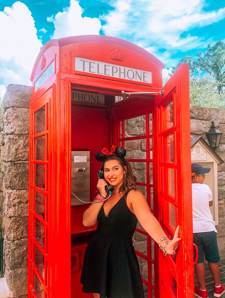 This may contain: a woman standing in a red phone booth