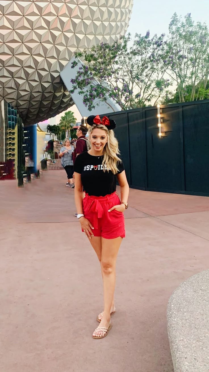 This may contain: a woman standing in front of the spaceship dome at disney's hollywood studios wearing minnie mouse ears