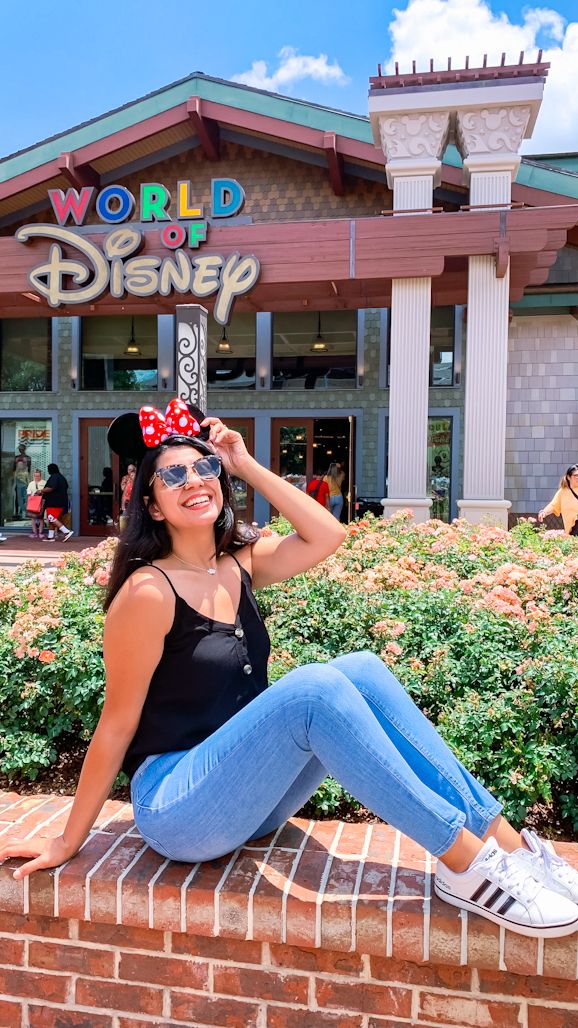 This may contain: a woman sitting on top of a brick wall in front of a disney world building