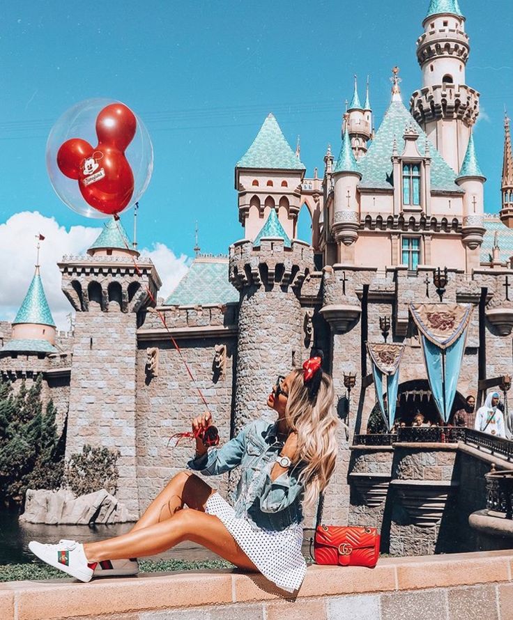 This may contain: a woman sitting on the edge of a wall in front of a castle with red balloons